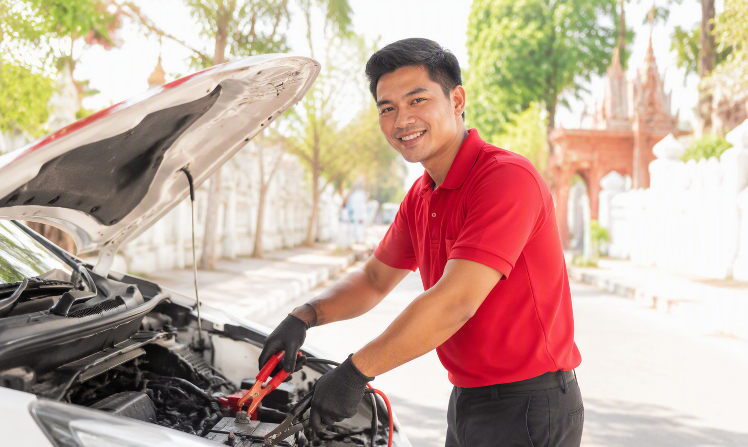 A Cambogara vetted mechanic jump-starting a car on a sunny Cambodian street